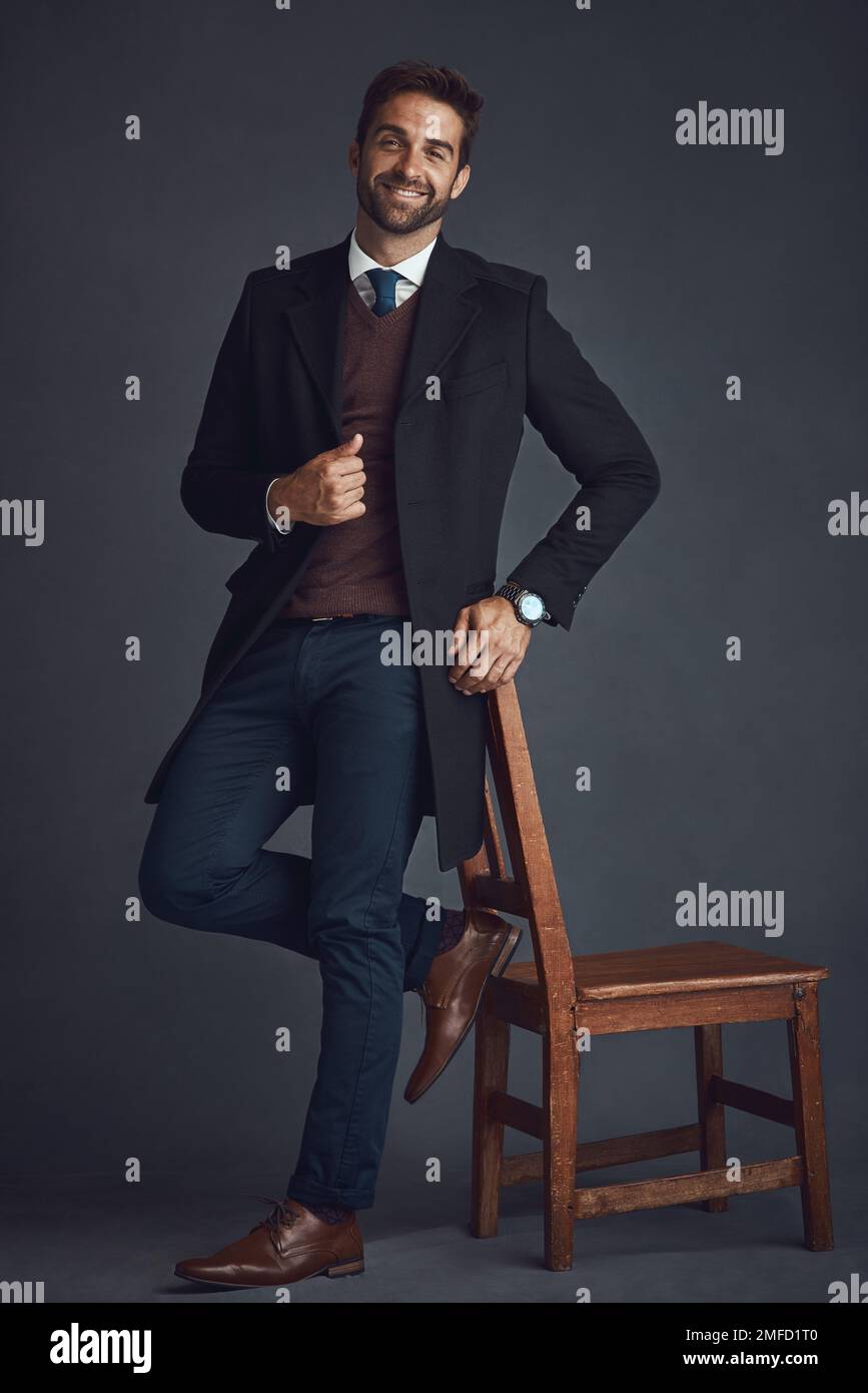 Indossala qualsiasi cosa ti faccia scoprire il meglio. Studio ritratto di un giovane uomo elegantemente vestito in piedi accanto a una sedia su uno sfondo grigio. Foto Stock