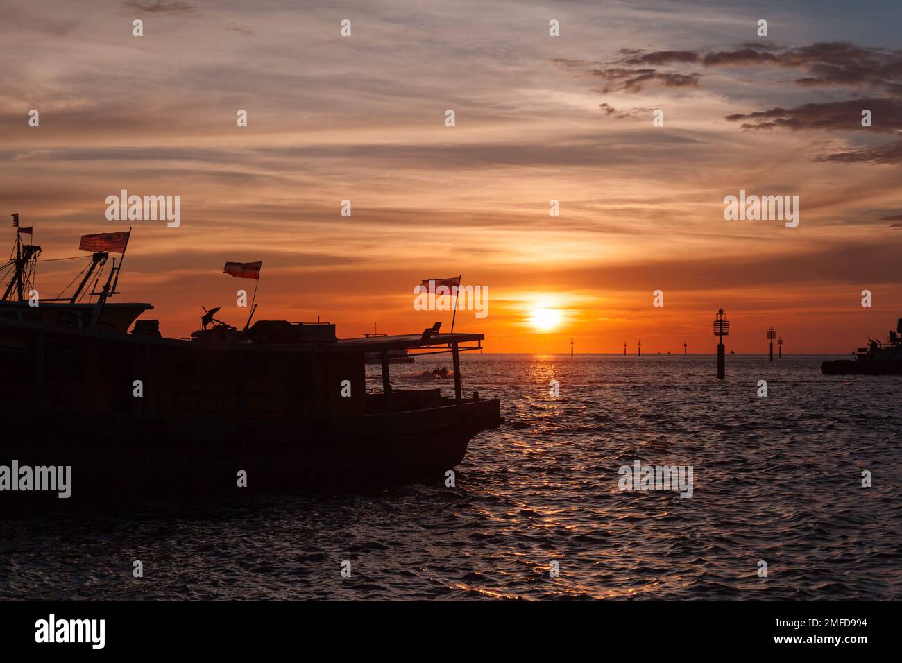 Silhouette di barche da pesca con bandiere malesi ormeggiate al KK Fish Market al tramonto Foto Stock