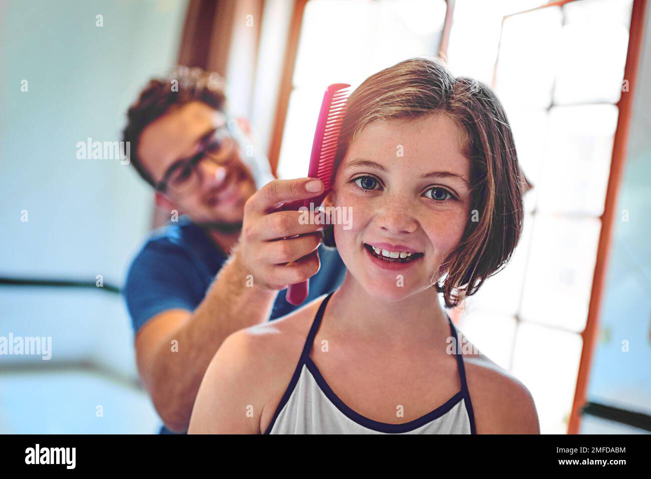 Preparatevi con un po' di aiuto da papà. un padre che pettina i capelli delle sue figlie a casa. Foto Stock