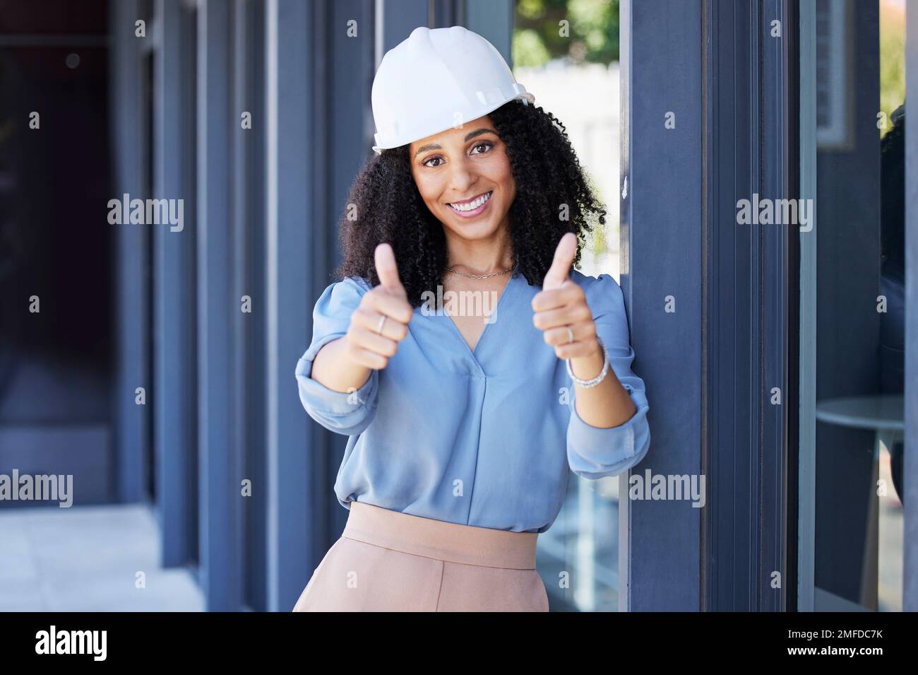 Donna nera, ritratto sorriso e pollici in su per la costruzione, costruzione o buon lavoro con elmetto per la sicurezza sul lavoro in loco. Felice afro americano femmina Foto Stock
