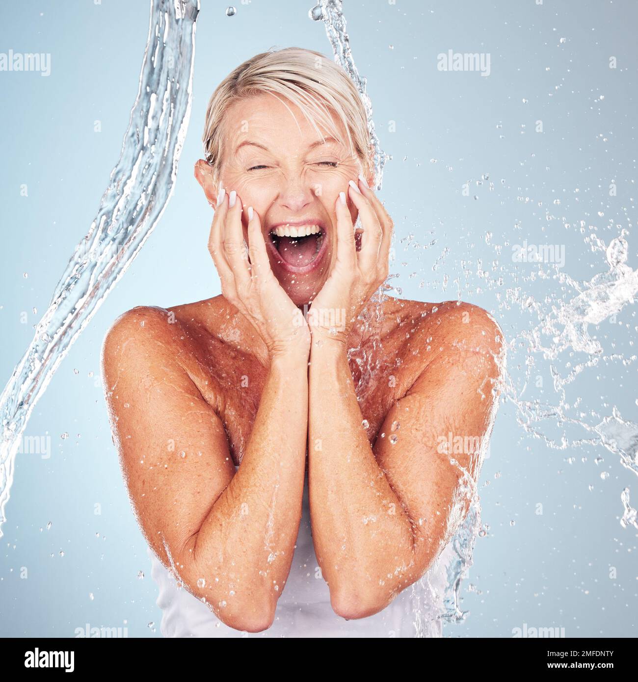 Cura della pelle, eccitato e ritratto di una donna con un spruzzi d'acqua isolato su uno sfondo blu. Cura di sé, felice e volto di un modello di bellezza anziano Foto Stock