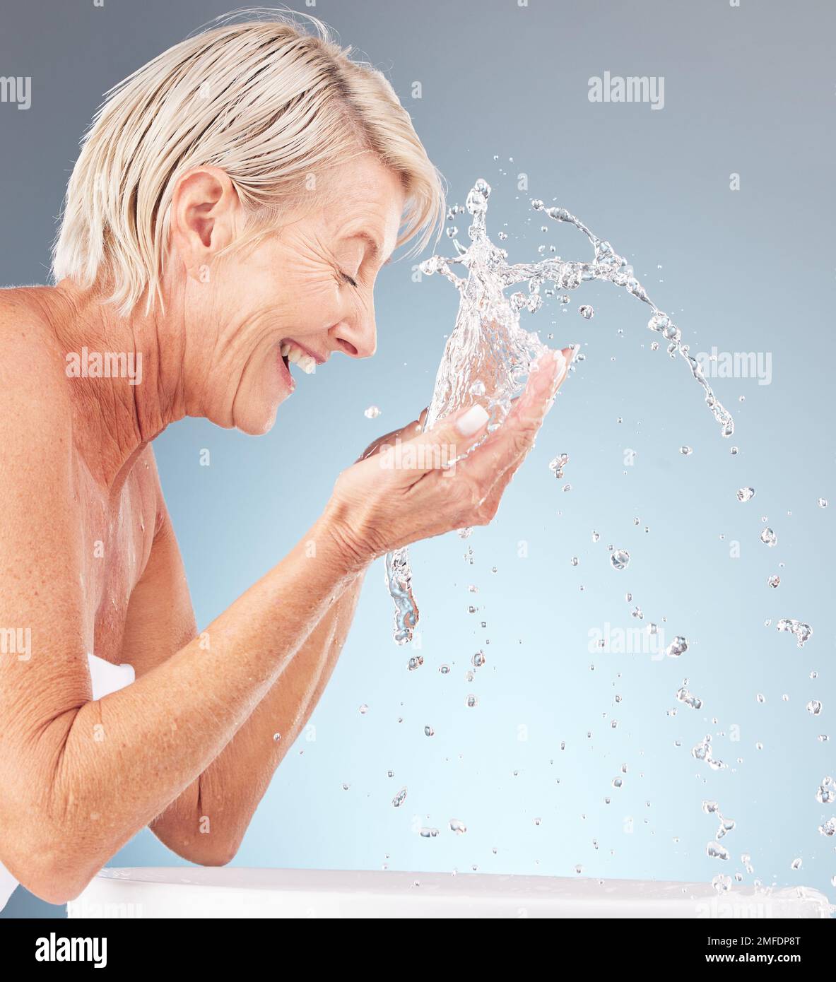 Donna anziana, pulizia viso e spruzzi d'acqua su sfondo studio per la bellezza, il benessere e la doccia. Modello felice, gocce per la cura della pelle del viso e lavaggio in Foto Stock