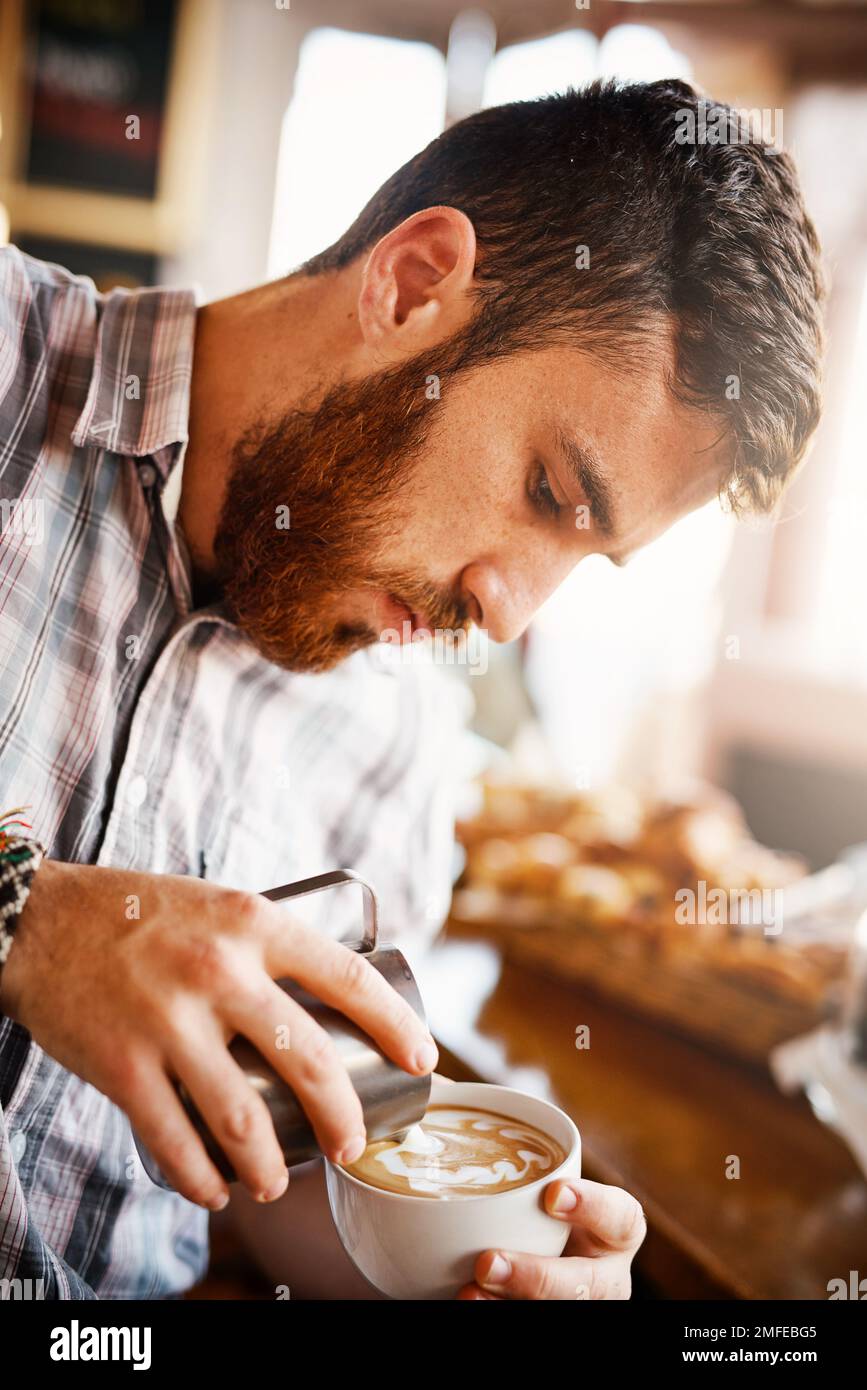 E' un'arte di per sé. Un colpo corto di un barista che versa latte schiumoso in una tazza di caffè caldo trasformandolo in un'immagine. Foto Stock