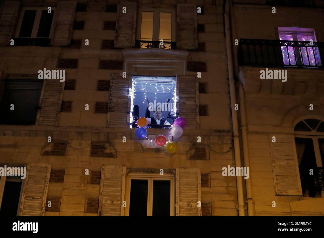 French tenor singer Stephane Senechal sings Christmas songs, at dusk, from his apartment window decorated with balloons during the partial lockdown, in Paris, Tuesday, Dec. 15, 2020. France on Tuesday is lifting a lockdown imposed on Oct. 30, but starts a new curfew at 20h00, local time, as infections are still high. (AP Photo/Francois Mori) Foto Stock