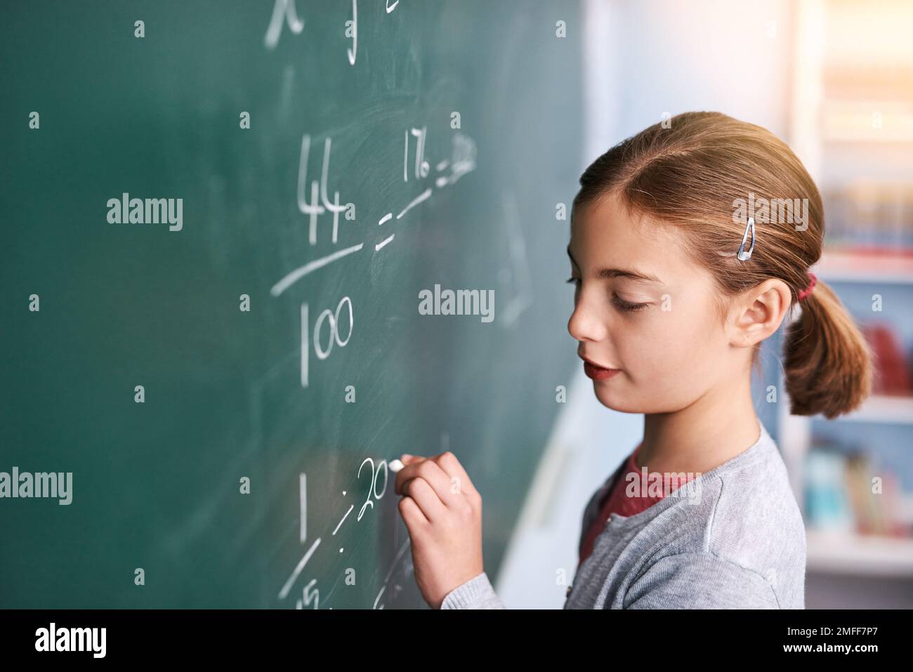 Questo dovrebbe essere corretto. un giovane bambino della scuola elementare focalizzato che scrive le risposte alle domande di matematica su una lavagna verde nella classe. Foto Stock