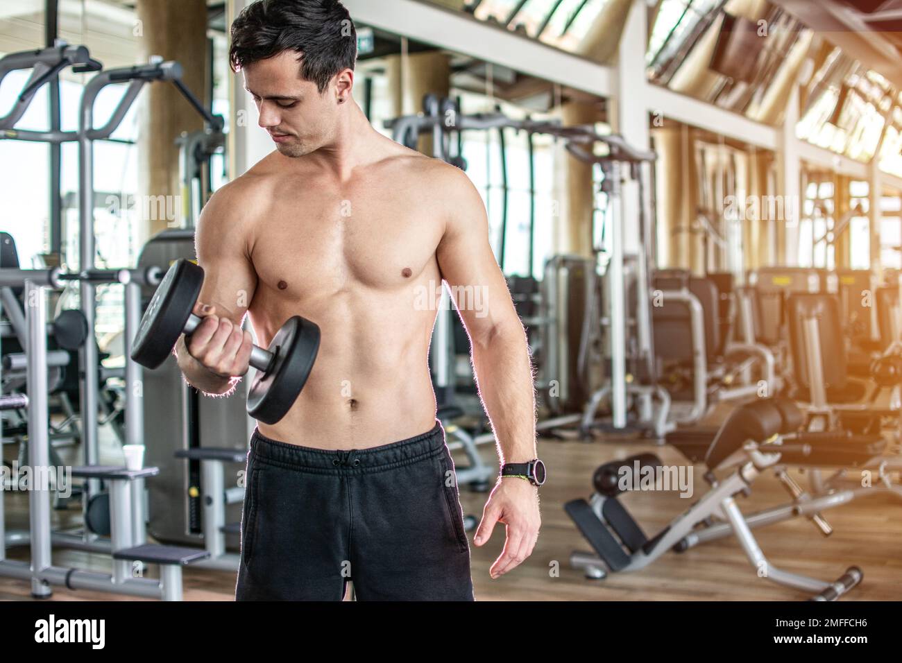 Giovane uomo che solleva il manubrio e si allena sul suo bicipite in palestra. Foto Stock