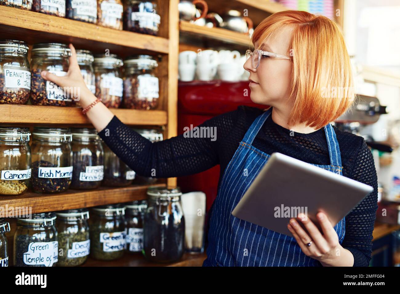 Lascia vedere che cosa vende e che cosa doesnt. una giovane donna che usa un tablet digitale mentre lavora in una caffetteria. Foto Stock