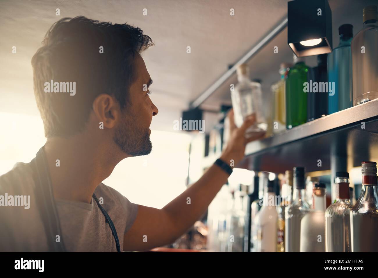 Il talento dietro una bevanda grande. un giovane uomo che guarda la merce sugli scaffali dietro un bancone bar. Foto Stock