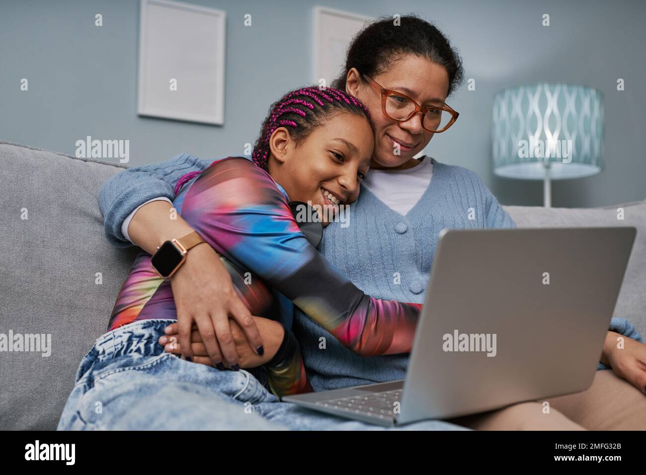 Ritratto di ragazza adolescente nera che usa il laptop mentre coccola con la mamma sul divano Foto Stock