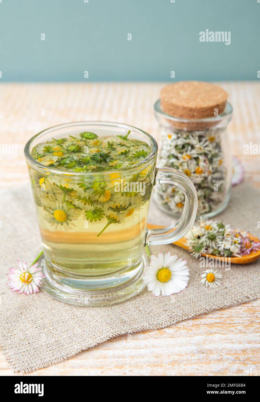 Pianta medicinale a base di erbe essiccata Daisy comune, noto anche come Bellis perennis. Fiori secchi in vaso di vetro e tè alle erbe in vetro, all'interno. Foto Stock