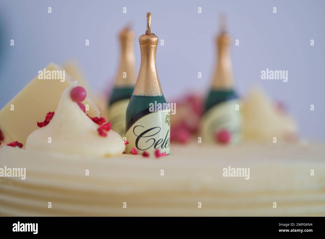 Candele di compleanno a forma di champagne seduti in cima a una torta di compleanno, con le lettere celebrare intorno a loro. un trio di candele Foto Stock