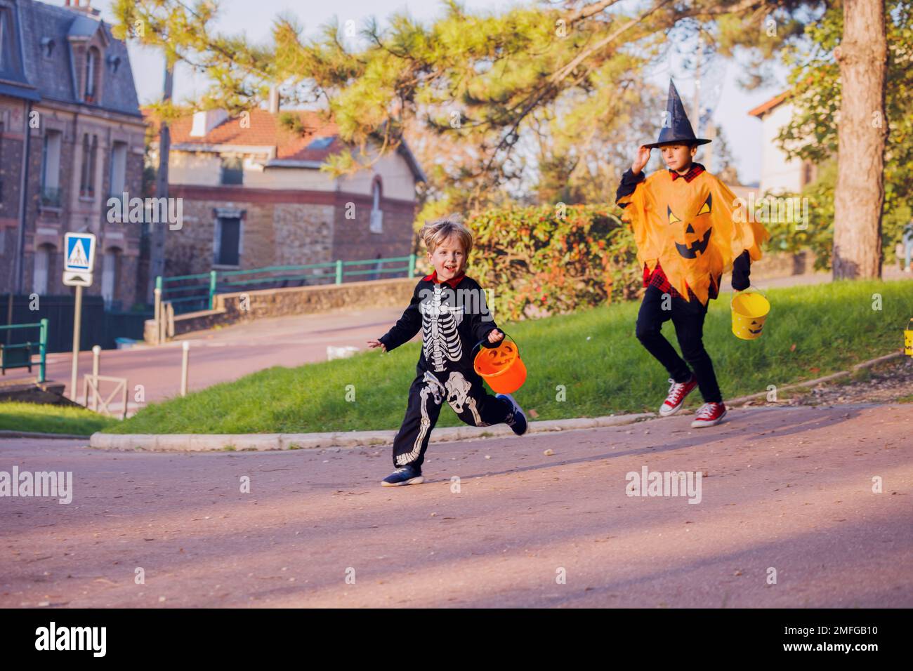 Due fratelli ragazzi corrono in costumi di Halloween tenere caramelle secchio Foto Stock