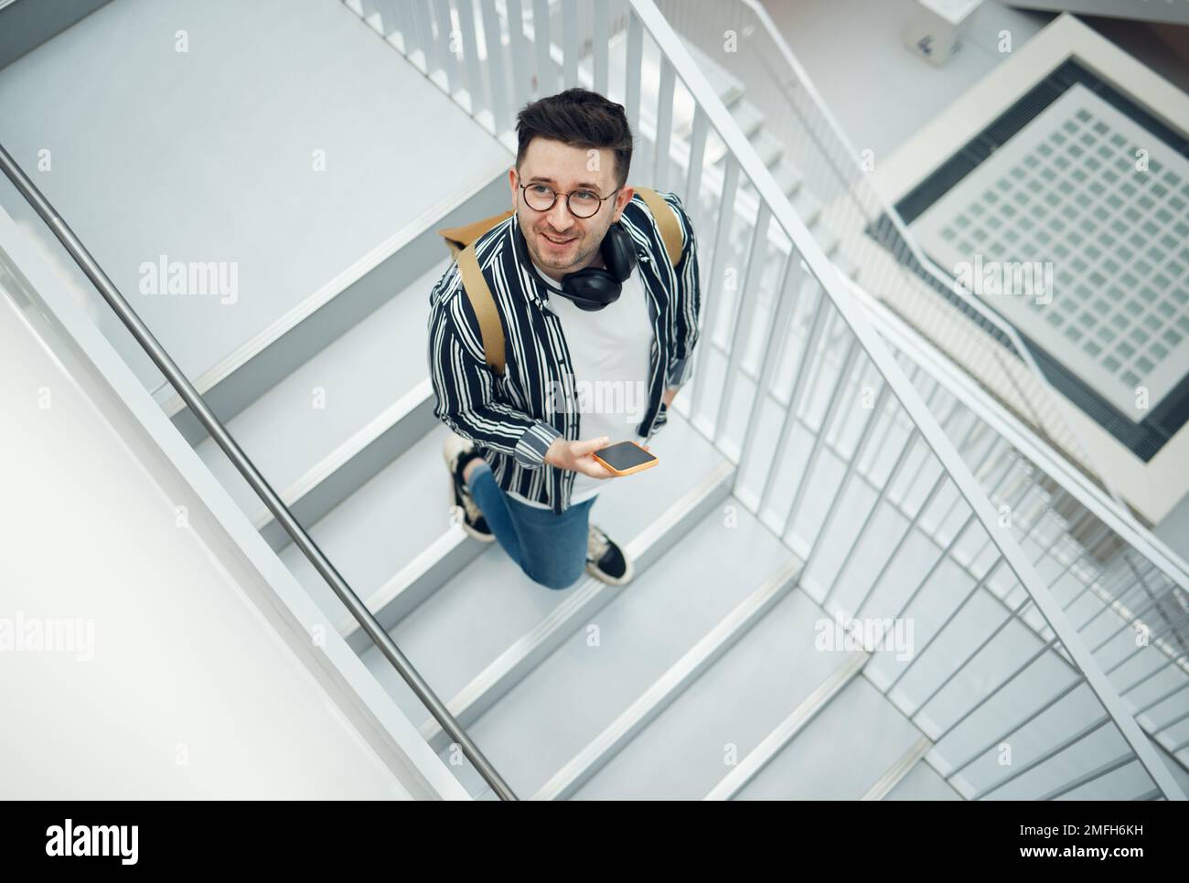 Felice, studente o startup uomo con telefono su scala per la ricerca su Internet, contenuti di social media o di networking. Sorridere, in alto o dipendente nerd su Foto Stock