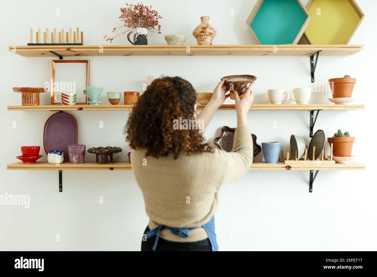 Felice giovane ceramista guardando via pensieroso mentre prende il calcio. Donna d'affari creativa che gestisce un negozio con prodotti in ceramica fatti a mano. Interno femminile Foto Stock