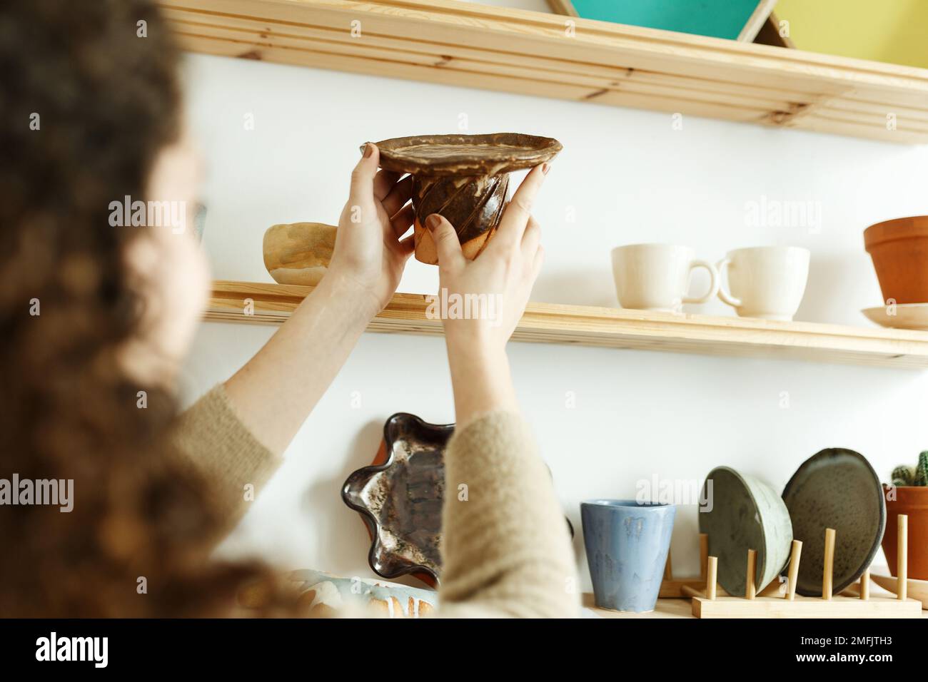 Felice giovane ceramista guardando via pensieroso mentre prende il calcio. Donna d'affari creativa che gestisce un negozio con prodotti in ceramica fatti a mano. Interno femminile Foto Stock