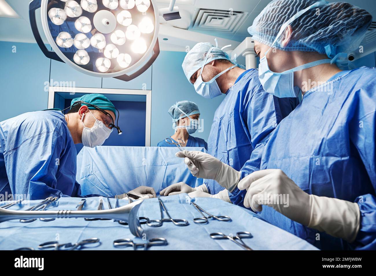 Infermiere chirurgico che fornisce forbici chirurgiche al chirurgo maschile durante il funzionamento in sala operatoria. Team chirurgico Foto Stock
