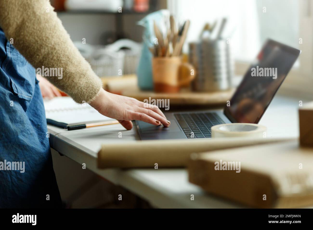 Donna tagliata in grembiule che lavora con il laptop in studio. Piccole imprese e imprenditorialità nell'arte, nel lavoro autonomo. Ufficio domestico. Foto Stock