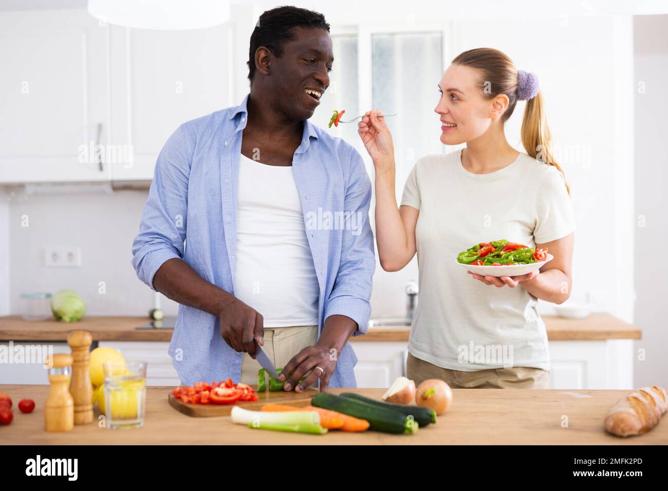 La moglie dà il sapore di insalata deliziosa nella cucina moderna a casa Foto Stock
