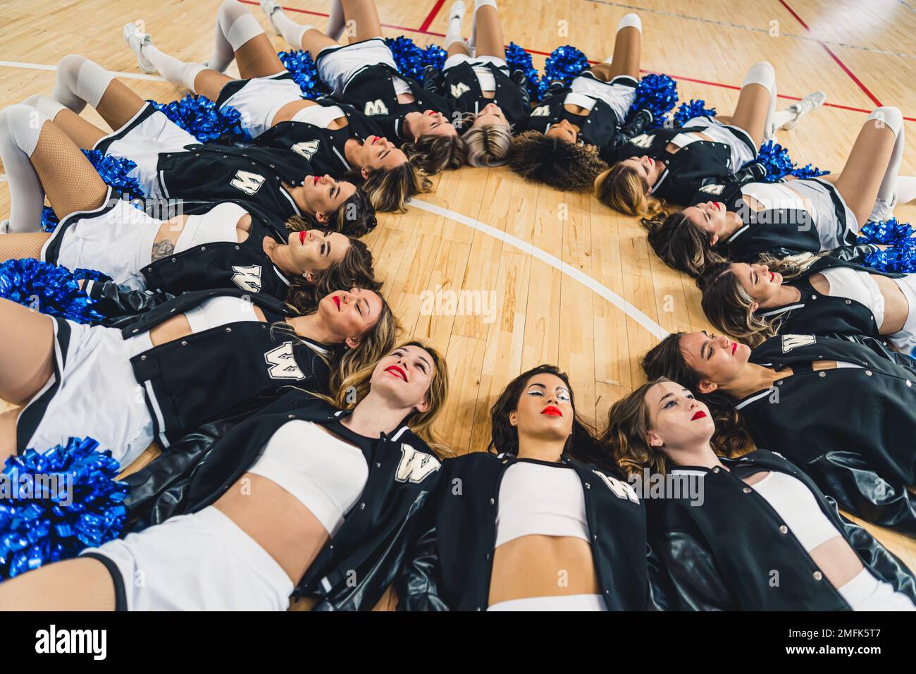 Cheerleaders femminile giacente in un cerchio sul campo da basket mentre tiene in mano i pom blu lucenti. Foto di alta qualità Foto Stock