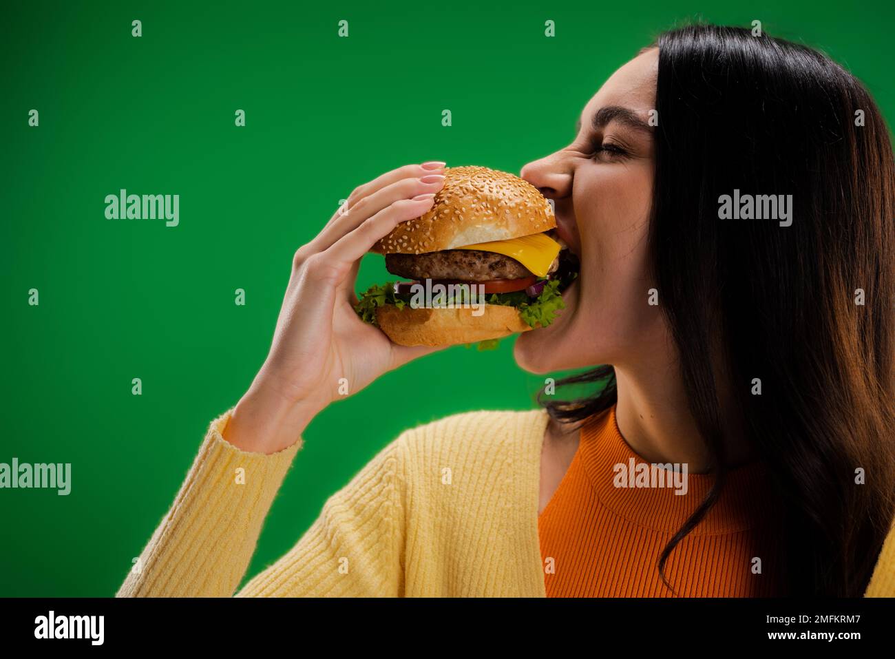 donna affamata mangiare delizioso hamburger isolato sul verde, immagine stock Foto Stock