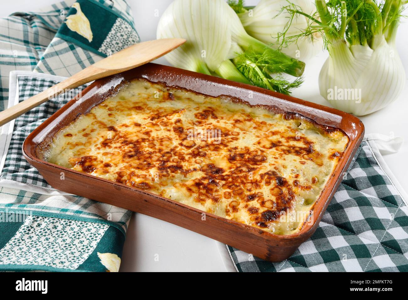 Finocchio al gratin al forno servito in un piatto bianco, con finocchio fresco nelle vicinanze Foto Stock