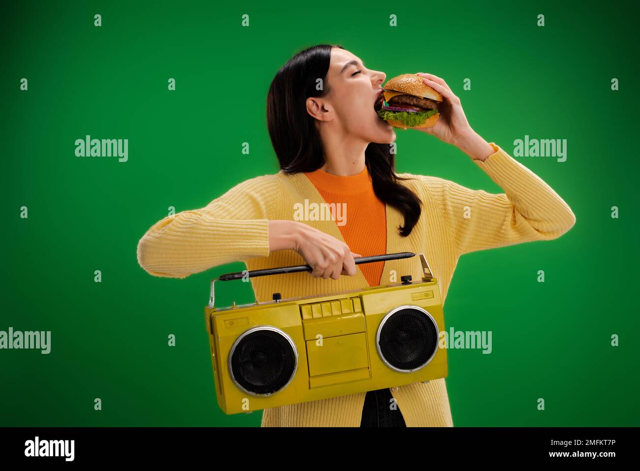 giovane e donna affamata con boombox mangiare gustoso hamburger isolato sul verde, immagine stock Foto Stock