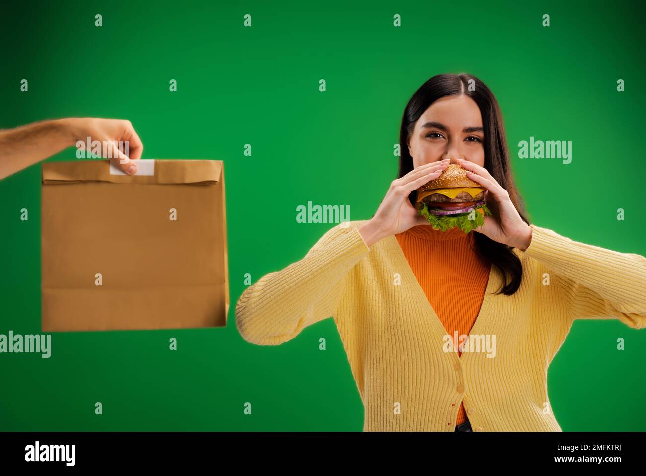 donna affamata mangiare delizioso hamburger vicino all'uomo con pacchetto di cibo isolato sul verde, immagine stock Foto Stock