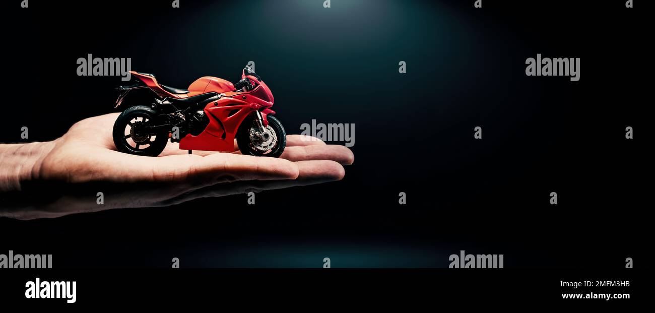 modello sportivo rosso in mano su sfondo scuro. acquista o noleggia una moto. banner con spazio di copia Foto Stock