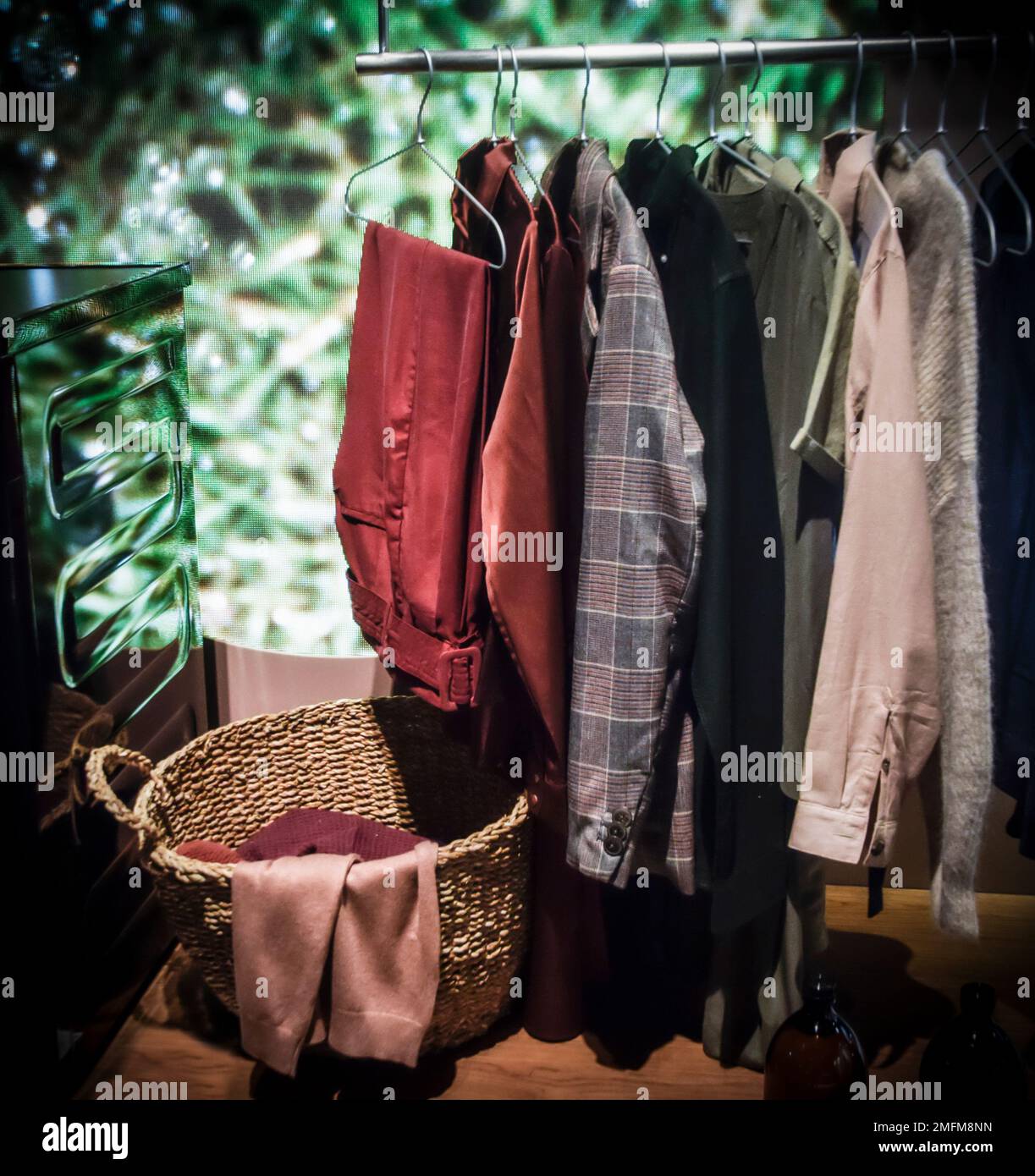 Una fila di abiti multicolore appesi accanto a un cesto della lavanderia Foto Stock