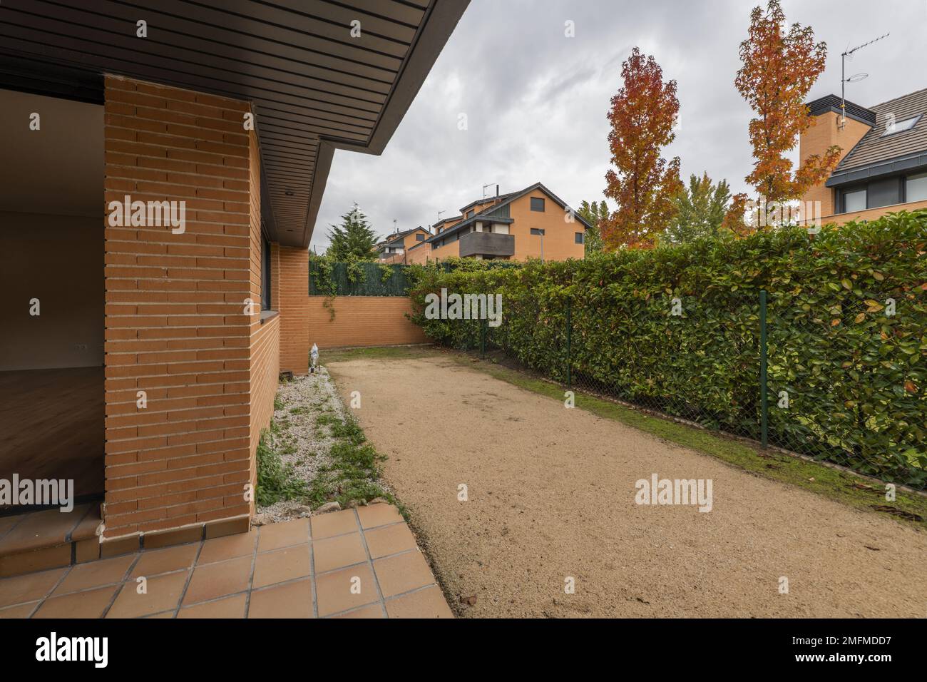 Patio di una casa semi-indipendente con pavimenti in gres marrone e terreno sabbioso con una siepe bushy che lo separa dai vicini Foto Stock