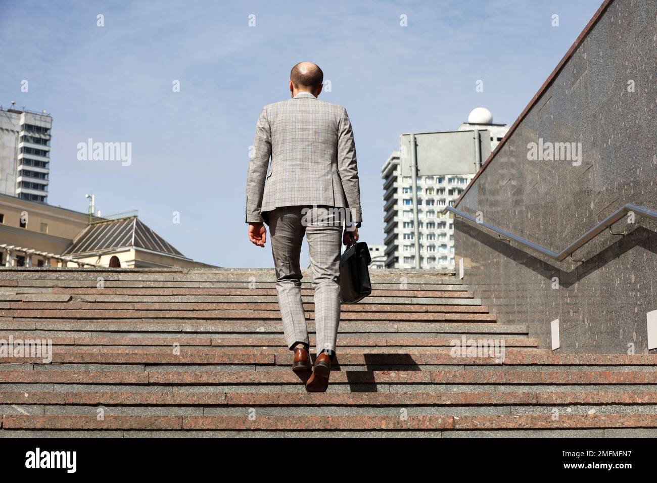 Uomo in una tuta da lavoro con valigetta in pelle scalinata scale in pietra in città, gambe maschili in movimento sui gradini. Concetto di carriera, successo Foto Stock