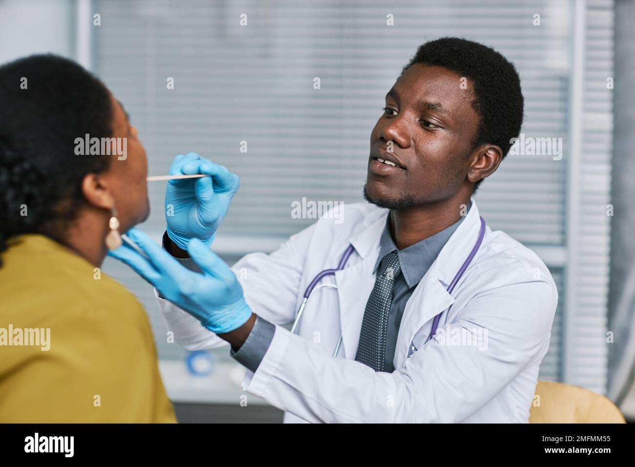 Ritratto del giovane medico nero che esamina il paziente in clinica e che fa controllo di influenza Foto Stock