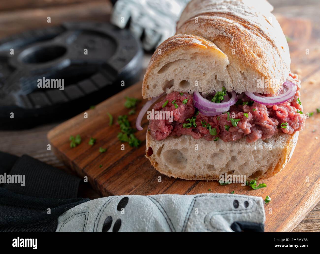 Muscolo costruzione Tatar o manzo crudo panino cannibale con prezzemolo e cipolle rosse su tavolo di legno. Primo piano e vista frontale Foto Stock