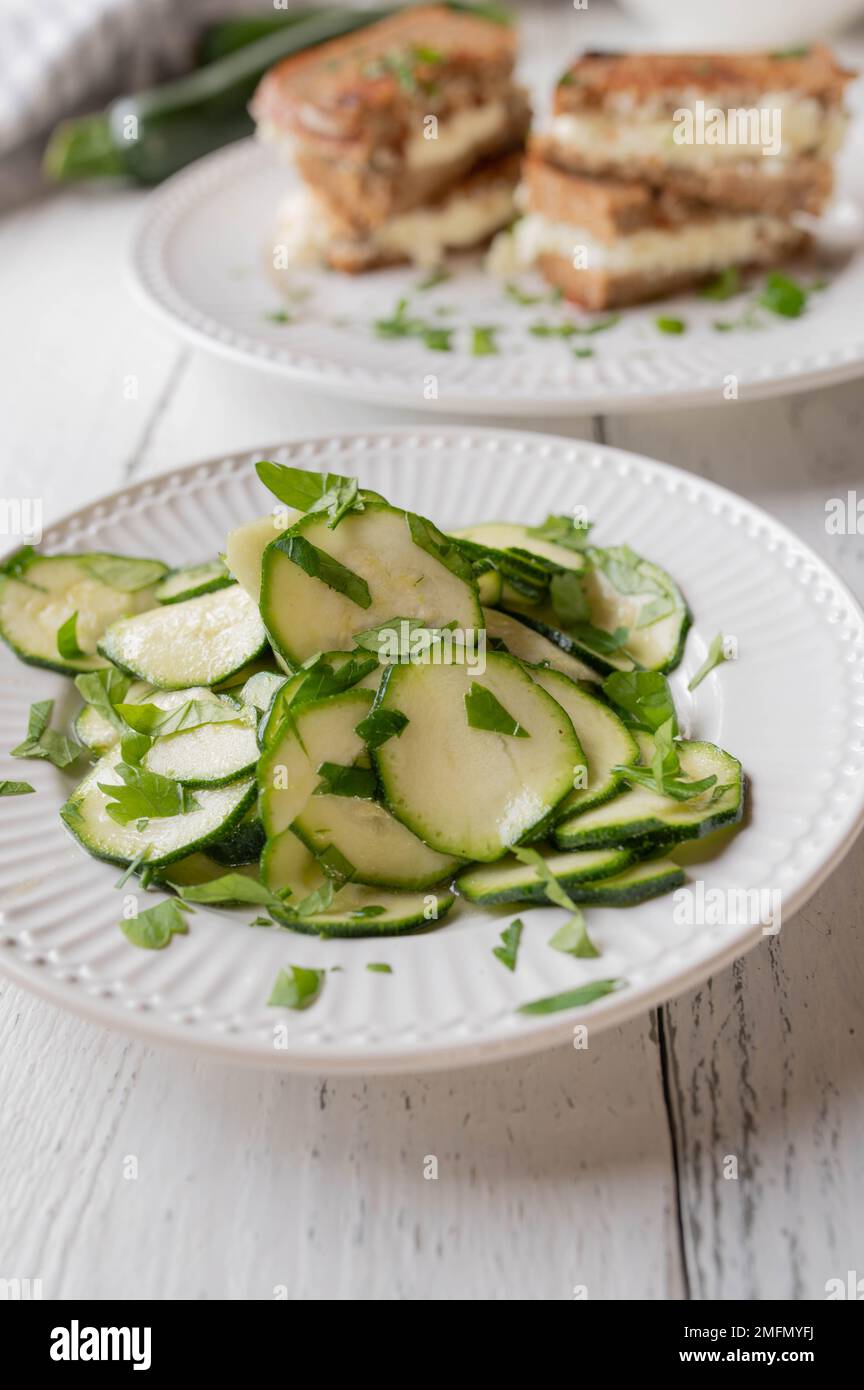 Insalata di zucchine marinata con olio d'oliva, aceto e miele. Servito come un sano panino contorno sul tavolo da cucina bianco. Vista frontale Foto Stock