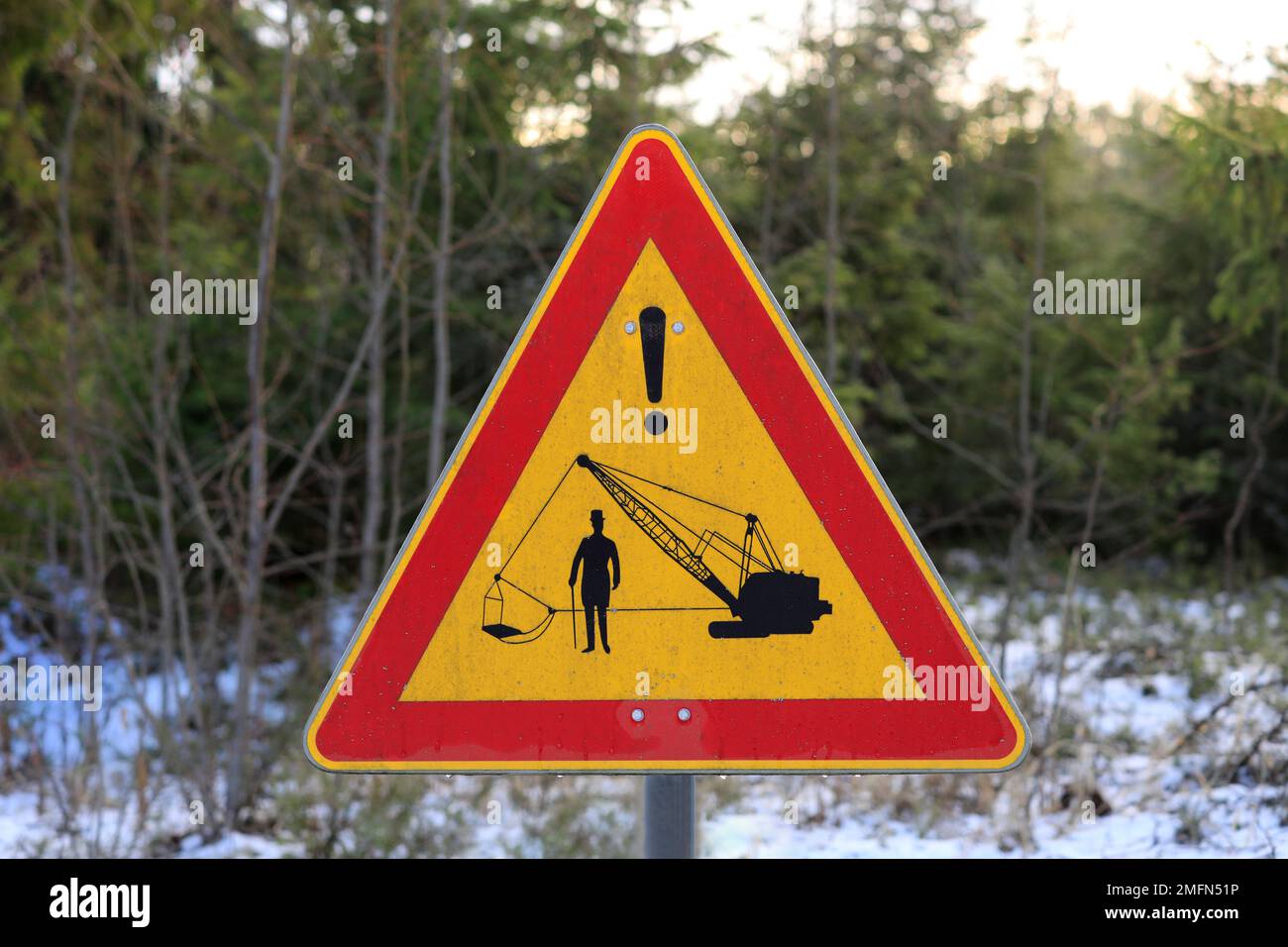 Segnaletica stradale personalizzata o segnaletica stradale con vecchio escavatore e un Signore con cappello e canna da zucchero su strada rurale in inverno. Finlandia 2023. Foto Stock
