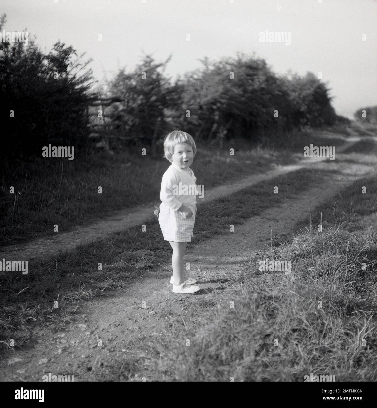1950s, storica, fuori in campagna, una dolce bambina in piedi su una pista agricola, girando la testa, forse controllando dove sono i suoi genitori, Inghilterra, Regno Unito. Foto Stock