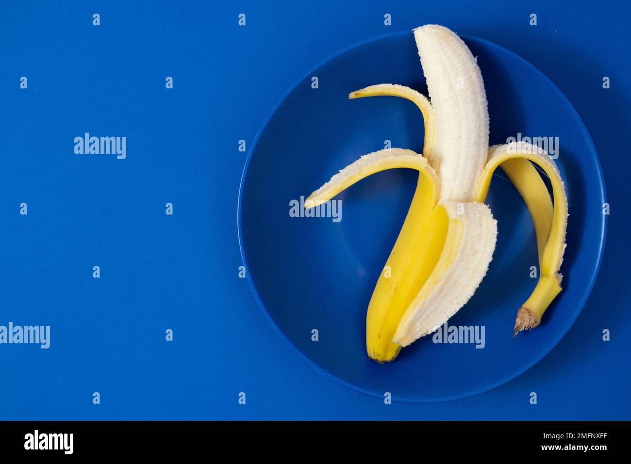 Banana semi sbucciata su sfondo blu scuro Foto Stock