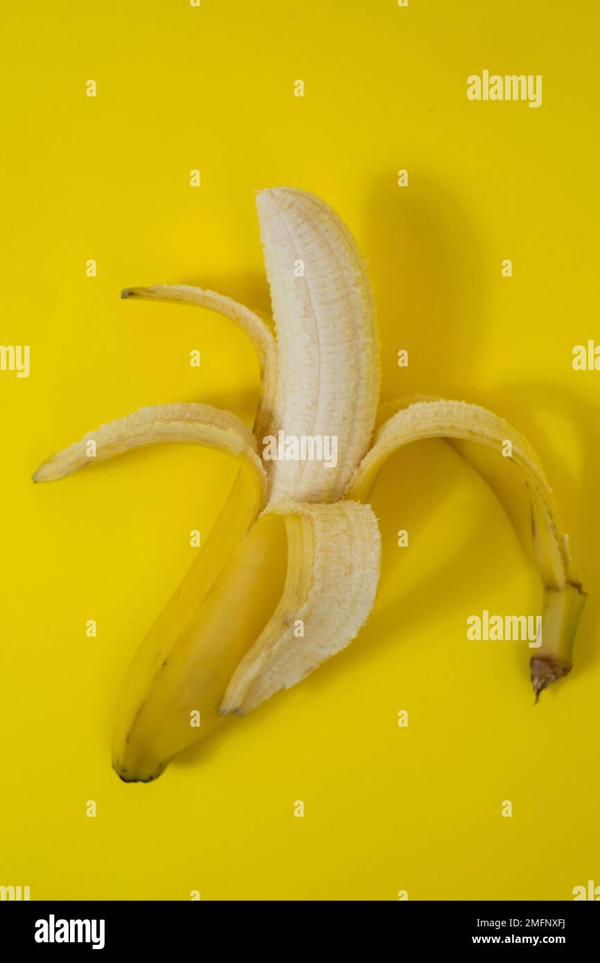 Banana semi sbucciata su sfondo giallo Foto Stock