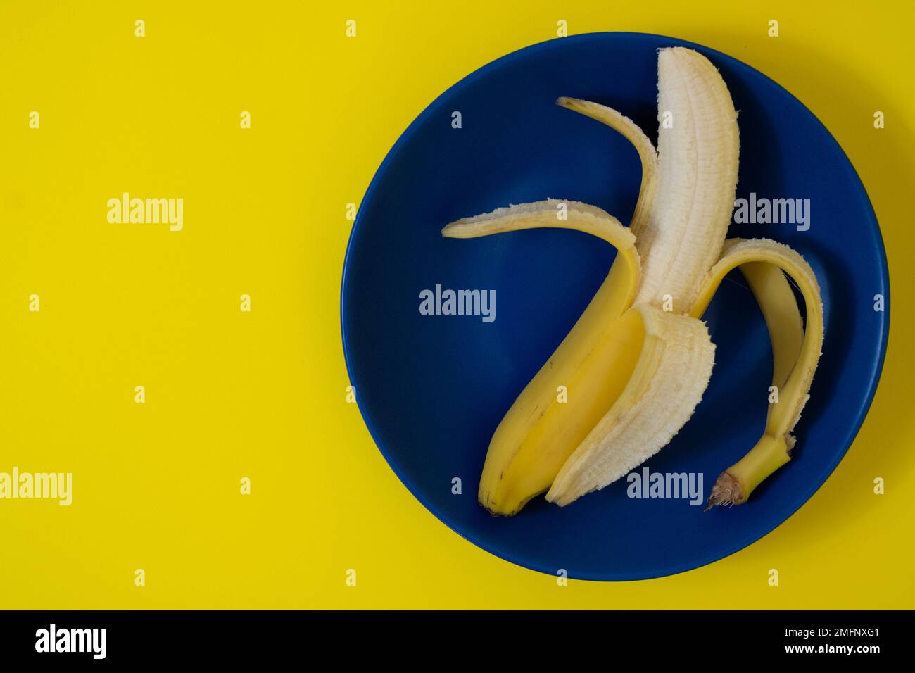 Banana semi sbucciata su piatto blu scuro Foto Stock