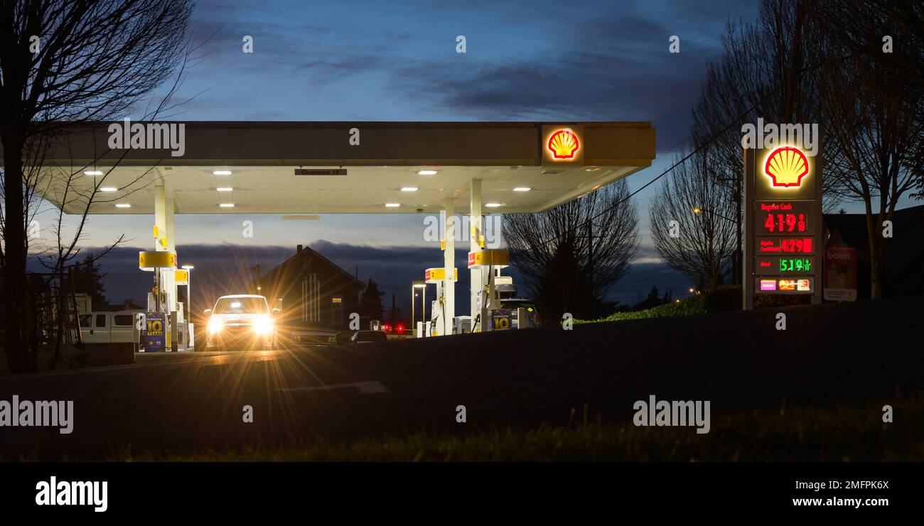 Snohomish, WA, USA - 23 gennaio 2023; vista notturna del piazzale della stazione di servizio Shell con travi di fari per auto parcheggiate alla pompa Foto Stock