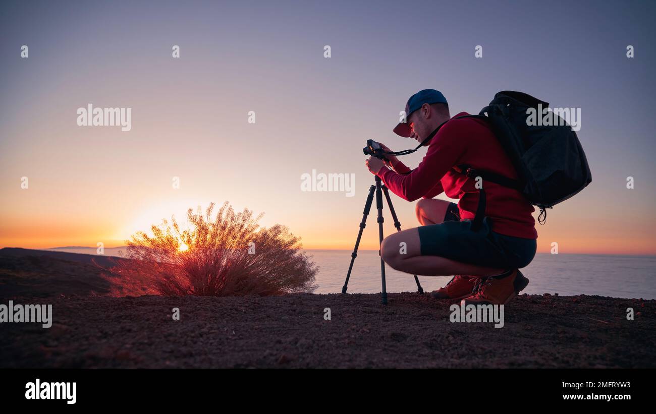 Fotografo con fotocamera su cavalletto al tramonto. Uomo durante fotografare il bellissimo paesaggio montano sopra le nuvole. Foto Stock