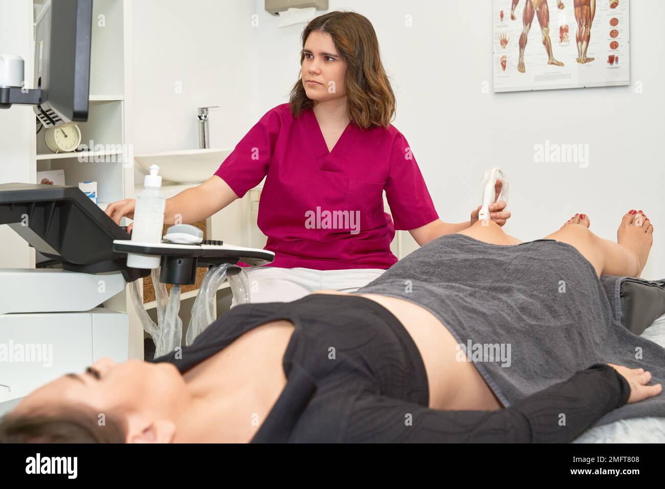 Medico donna che esegue l'ecografia del ginocchio al paziente sdraiato sul tavolo con apparecchiature ecografiche. Foto Stock