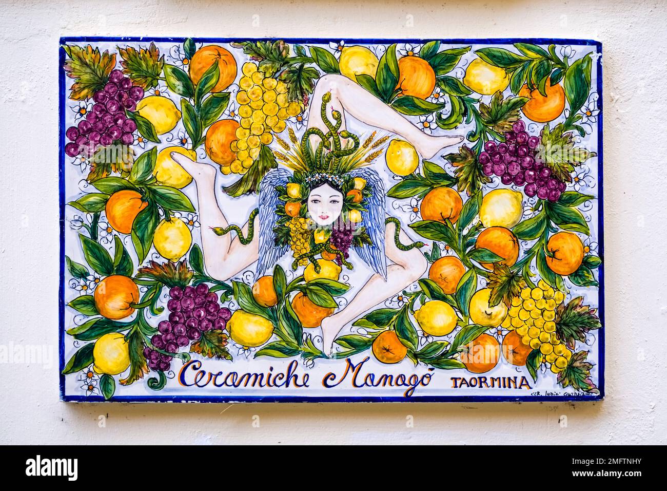 Muro di casa in uno dei vicoli della destinazione turistica di Taormina con una Trinacria, simbolo a tre zampe della Sicilia. Foto Stock