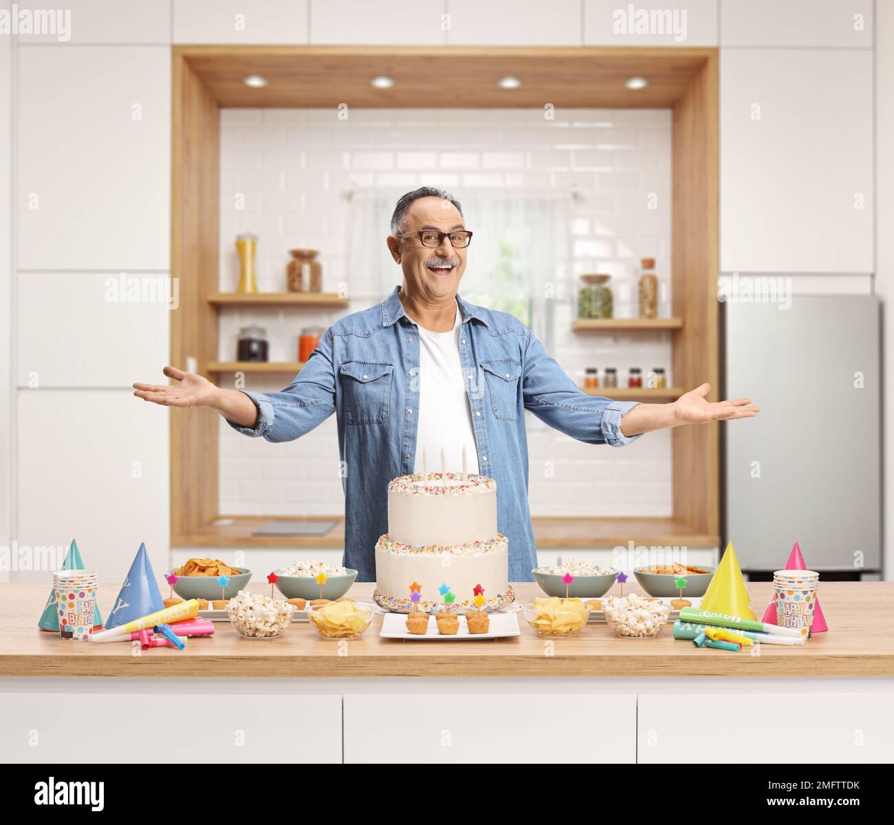 Uomo maturo con una torta in piedi all'interno di una cucina e sorridente Foto Stock