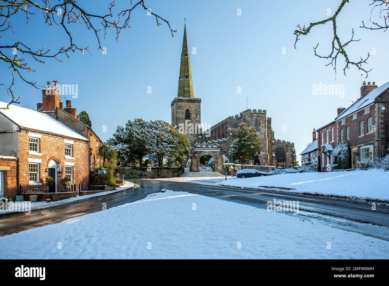 Chiesa di Santa Maria ad Astbury vicino a Congleton Cheshire Inghilterra con i cottage sul verde villaggio coperto di neve in inverno Foto Stock