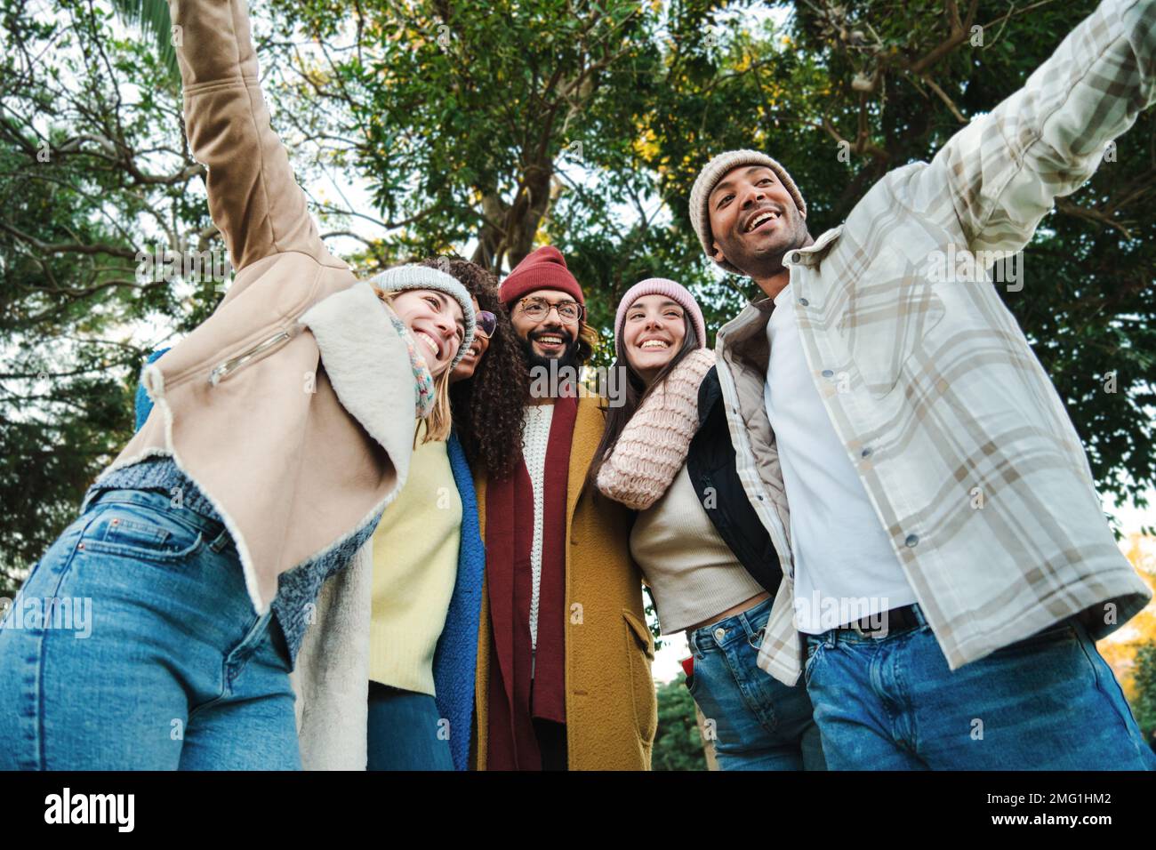 Un gruppo di giovani amici multirazziali che si divertono insieme in un parco durante le attività del fine settimana autunnale indossando cappotti e cappelli. Cinque persone felici sorridendo e camminando all'aperto. Concetto di stile di vita. Foto di alta qualità Foto Stock