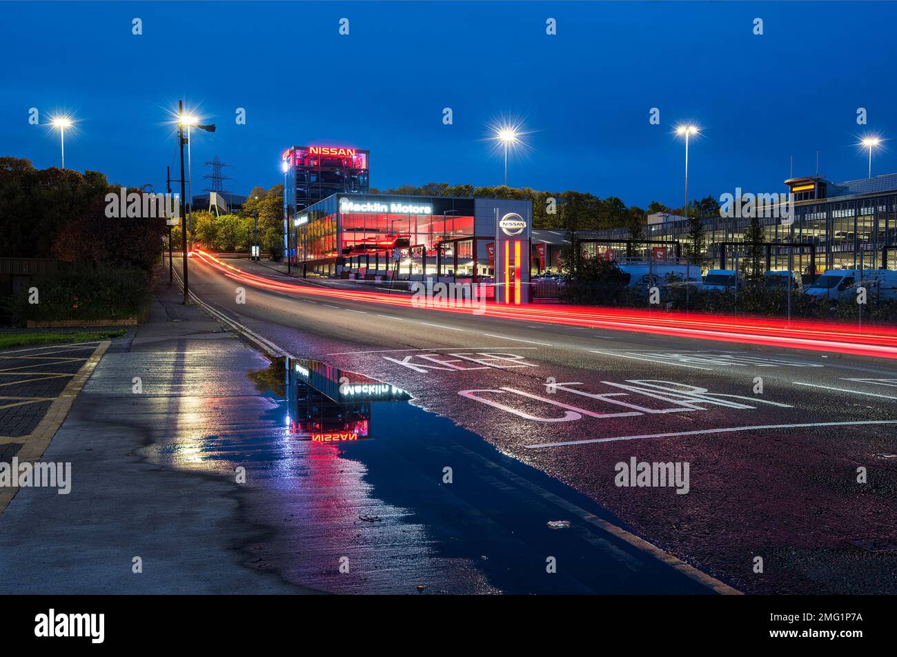 Riflessi dallo showroom di auto in acqua piovana di notte su Glasgow Road. Foto Stock