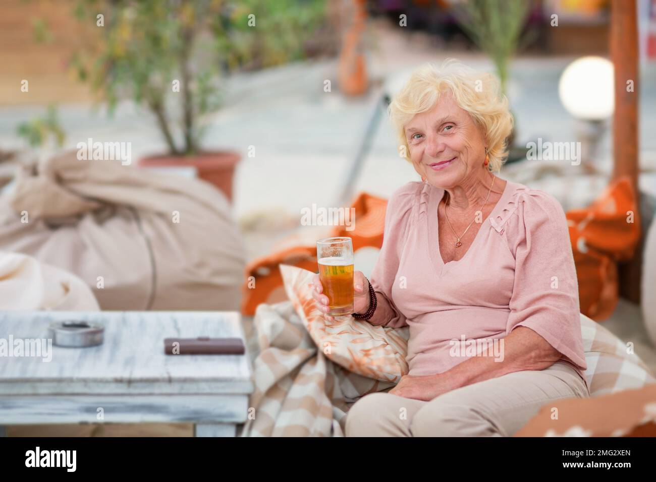 Donna matura seduta a un tavolo in un bar estivo e bere birra Foto Stock