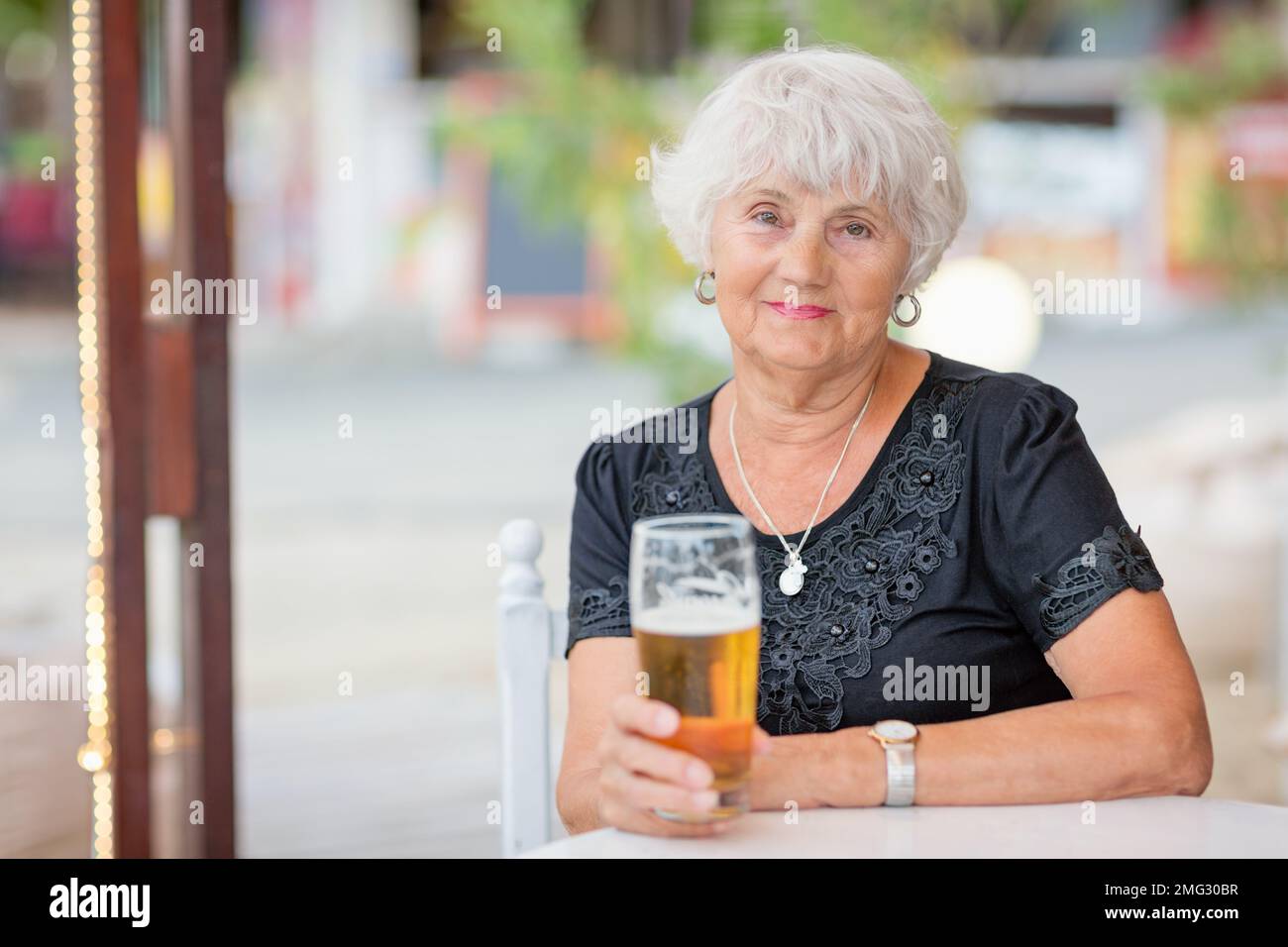 Donna matura seduta a un tavolo in un bar estivo e bere birra Foto Stock