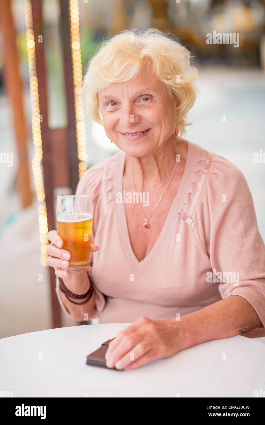 Donna matura seduta a un tavolo in un bar estivo e bere birra Foto Stock
